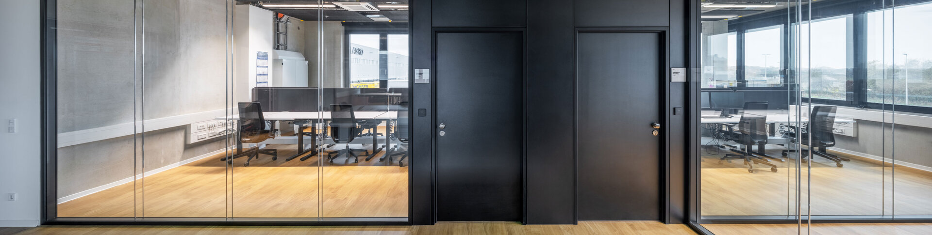Rahmenloses Glastrennwandsystem im Büro mit schwarzen Volltüren und schwarzen Leisten